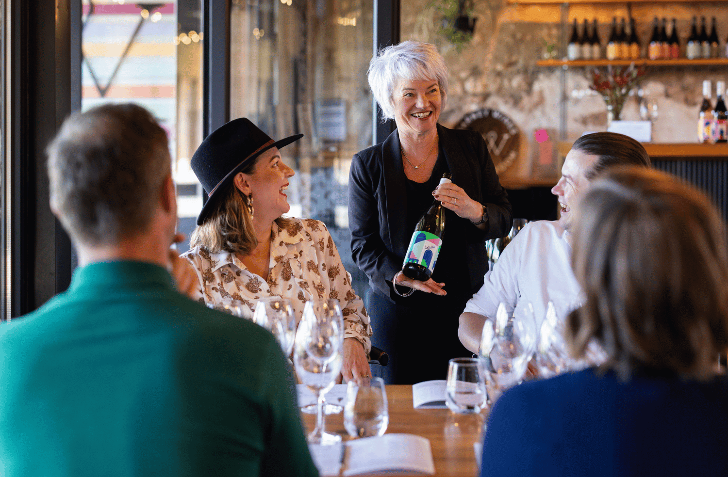 Group of people at a wine tasting event with a hostess holding a bottle of Varney Wines 'Entrada' Vermentino.