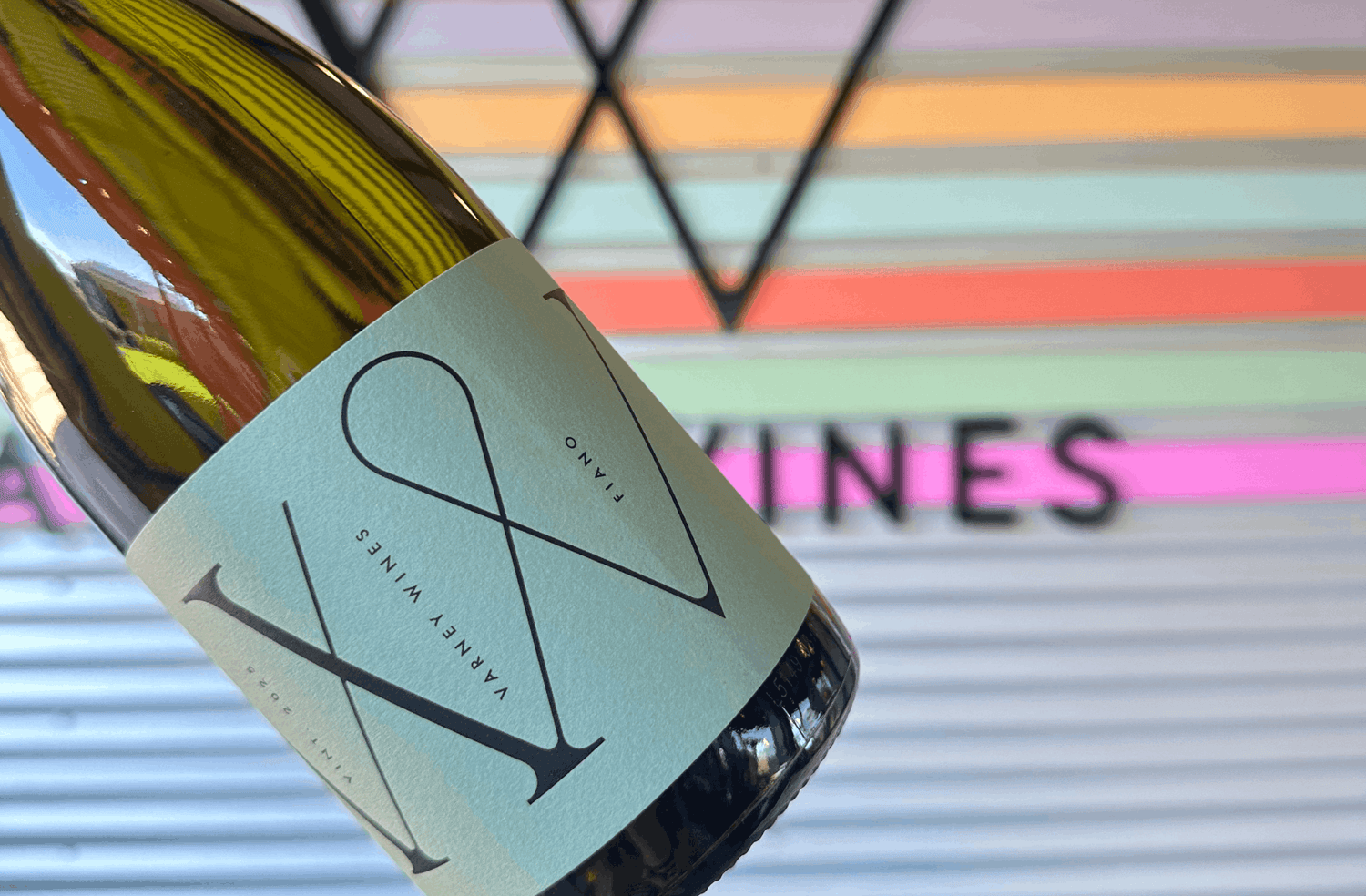 Close up of Varney Wines Fiano being held in front of the coloured sign at the Varney Wines Cellar Door and Tasting Room in McLaren Vale.